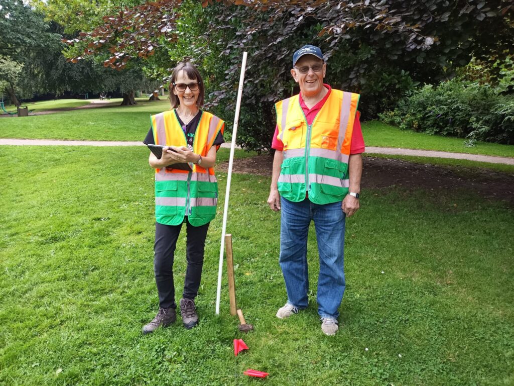 Two urban forest volunteers, smiling whilst measuring the height of a tree.